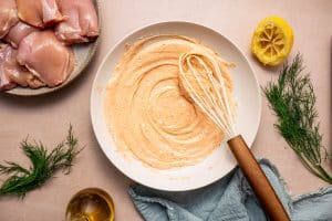 Mixing Greek yogurt marinade with olive oil, lemon juice, oregano, paprika, and salt in a large bowl.