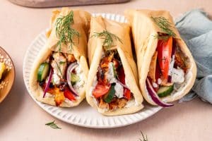 Warm pita breads filled with freshly sliced chicken gyros, creamy tzatziki sauce, juicy tomato wedges, cucumber slices, red onions, and a sprinkle of feta cheese, ready to serve.