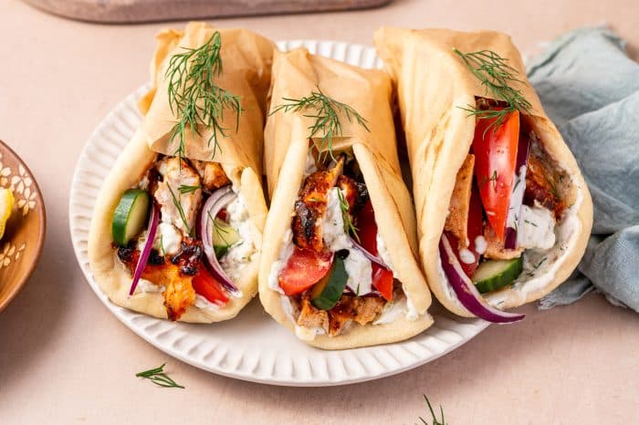 Warm pita breads filled with freshly sliced chicken gyros, creamy tzatziki sauce, juicy tomato wedges, cucumber slices, red onions, and a sprinkle of feta cheese, ready to serve.
