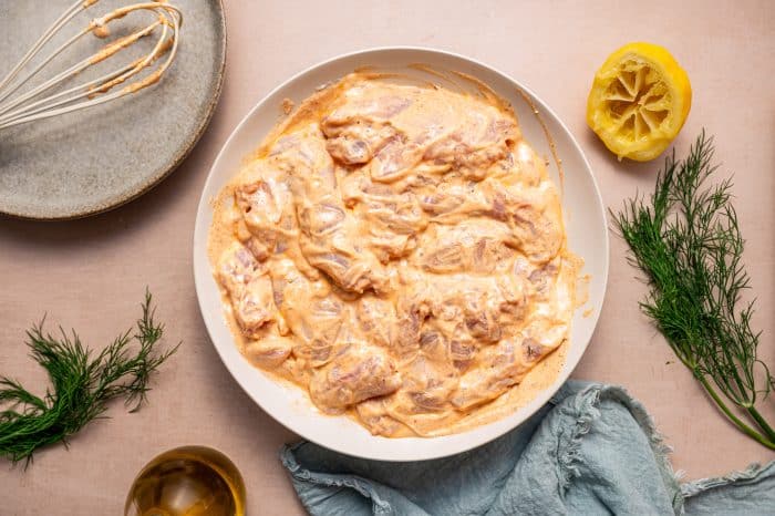 Marinated chicken thighs thoroughly coated in creamy yogurt marinade, placed in a bowl.