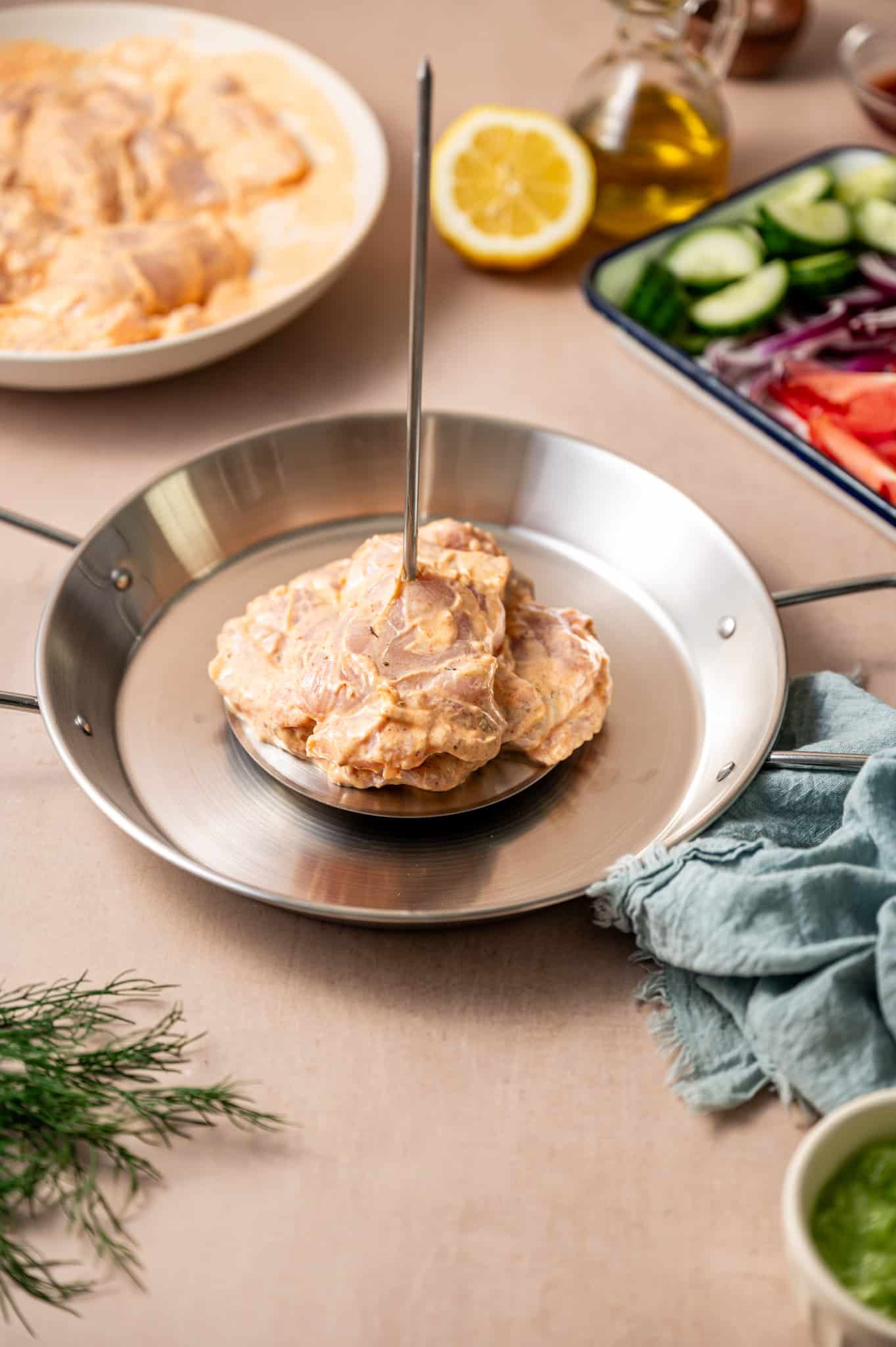 Chicken thigh pieces marinated in spiced yogurt being threaded on a vertical spit.