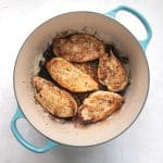 Golden pan-seared chicken cutlets in a turquoise-handled Dutch oven.