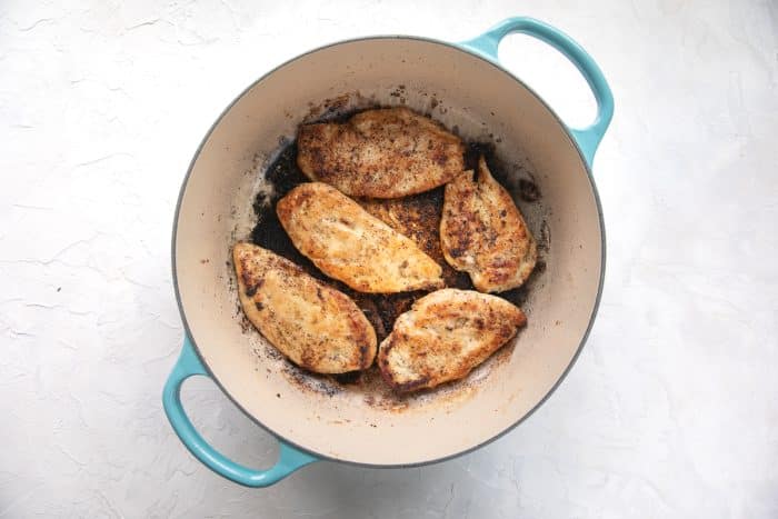 Golden pan-seared chicken cutlets in a turquoise-handled Dutch oven.