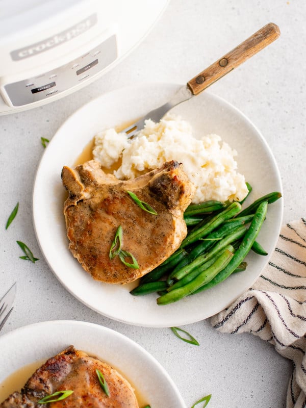 Juicy pork chop topped with thickened sauce on a plate with mashed potatoes and and green beans.