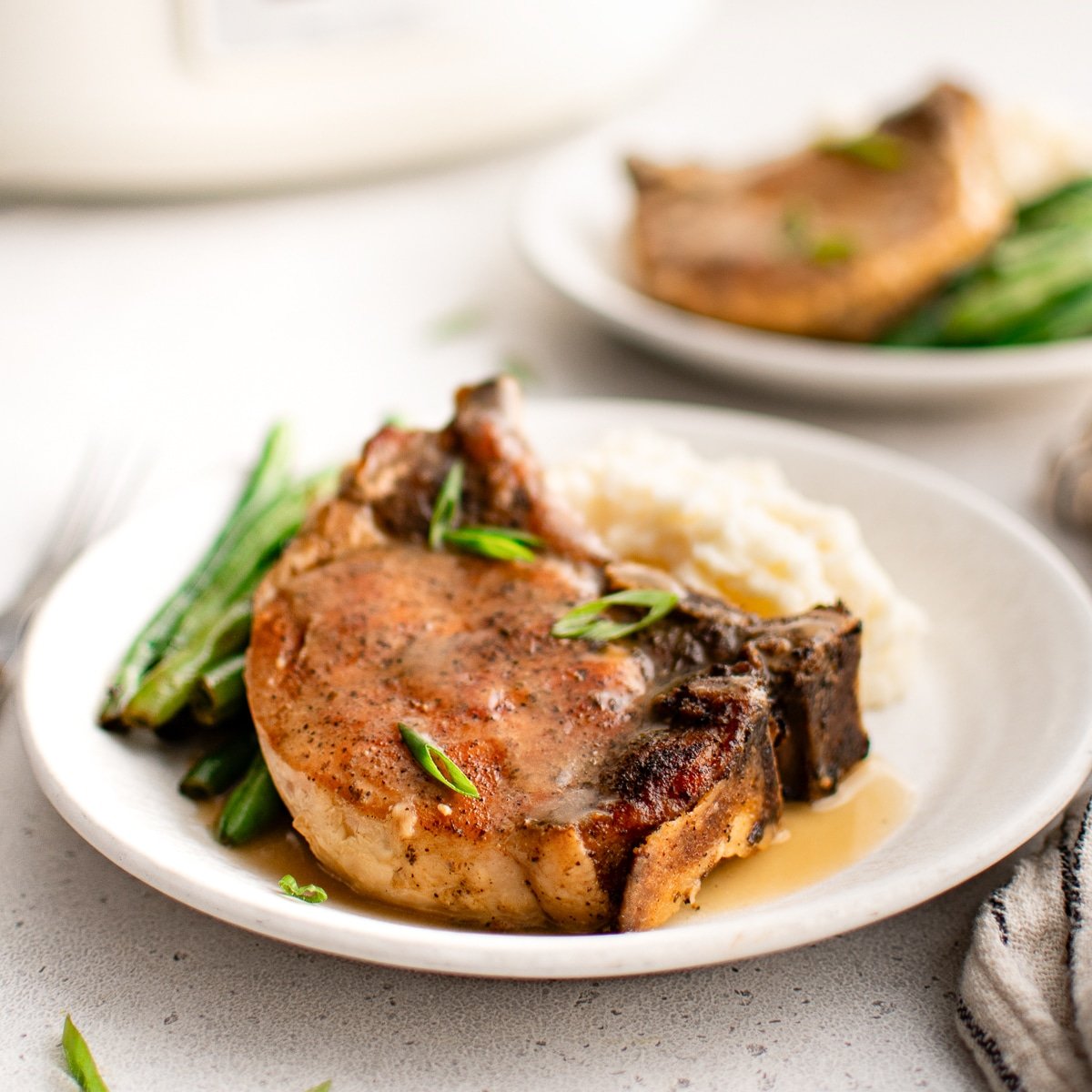Juicy pork chop topped with thickened sauce on a plate with mashed potatoes and and green beans.
