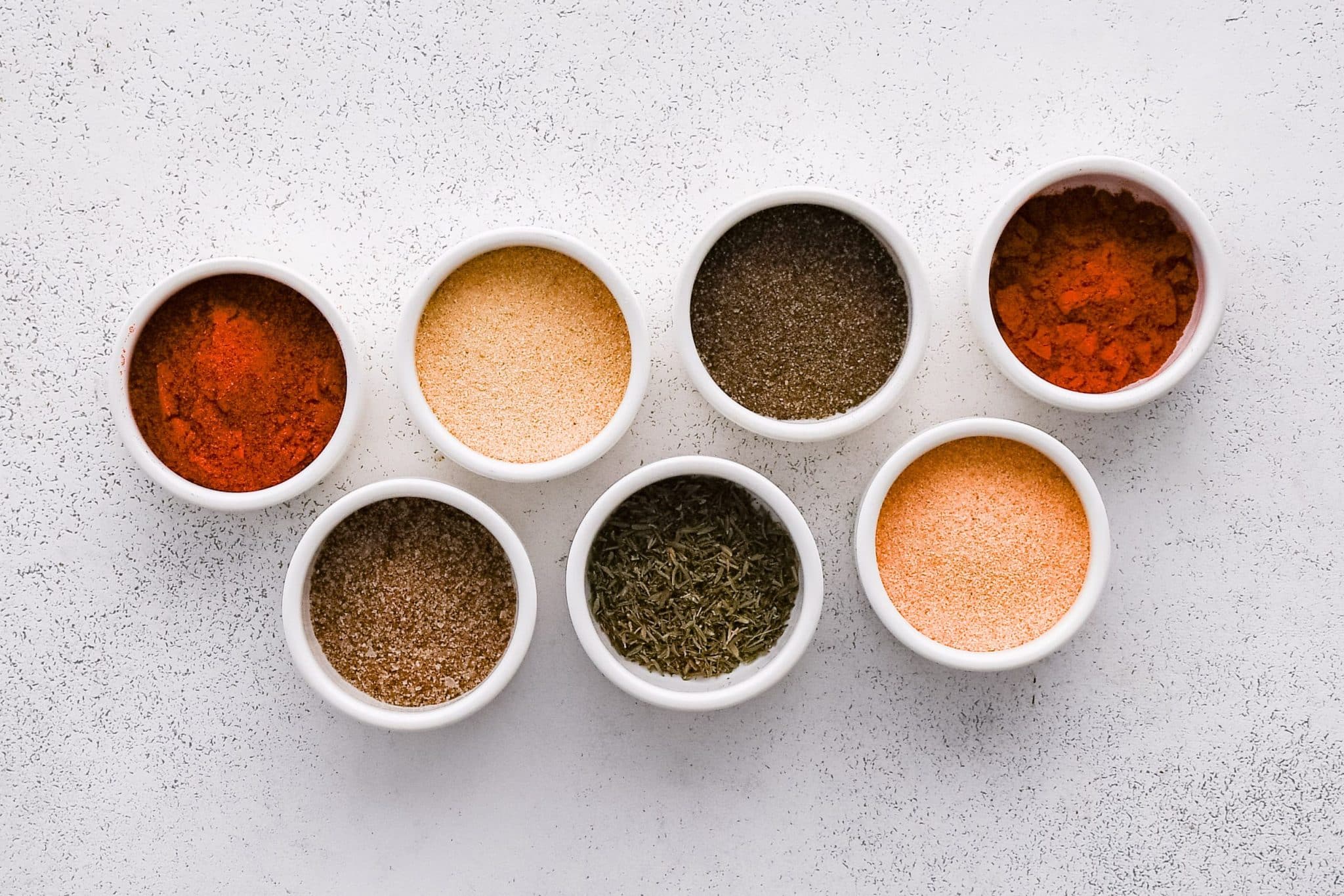 All of the ingredients for homemade Cajun seasoning presented in individual measuring cups and ramekins.