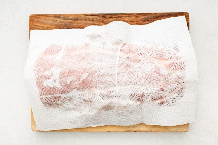 Pork loin roast on a large wooden cutting board covered with a paper towel.