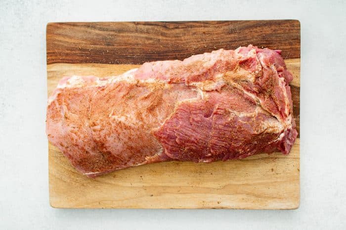 Pork loin roast on a large wooden cutting board coated in a homemade dry spice rub.