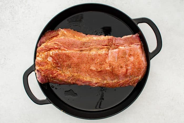 The seasoned pork loin is in a cast-iron skillet on the stovetop, searing to develop a golden-brown crust.