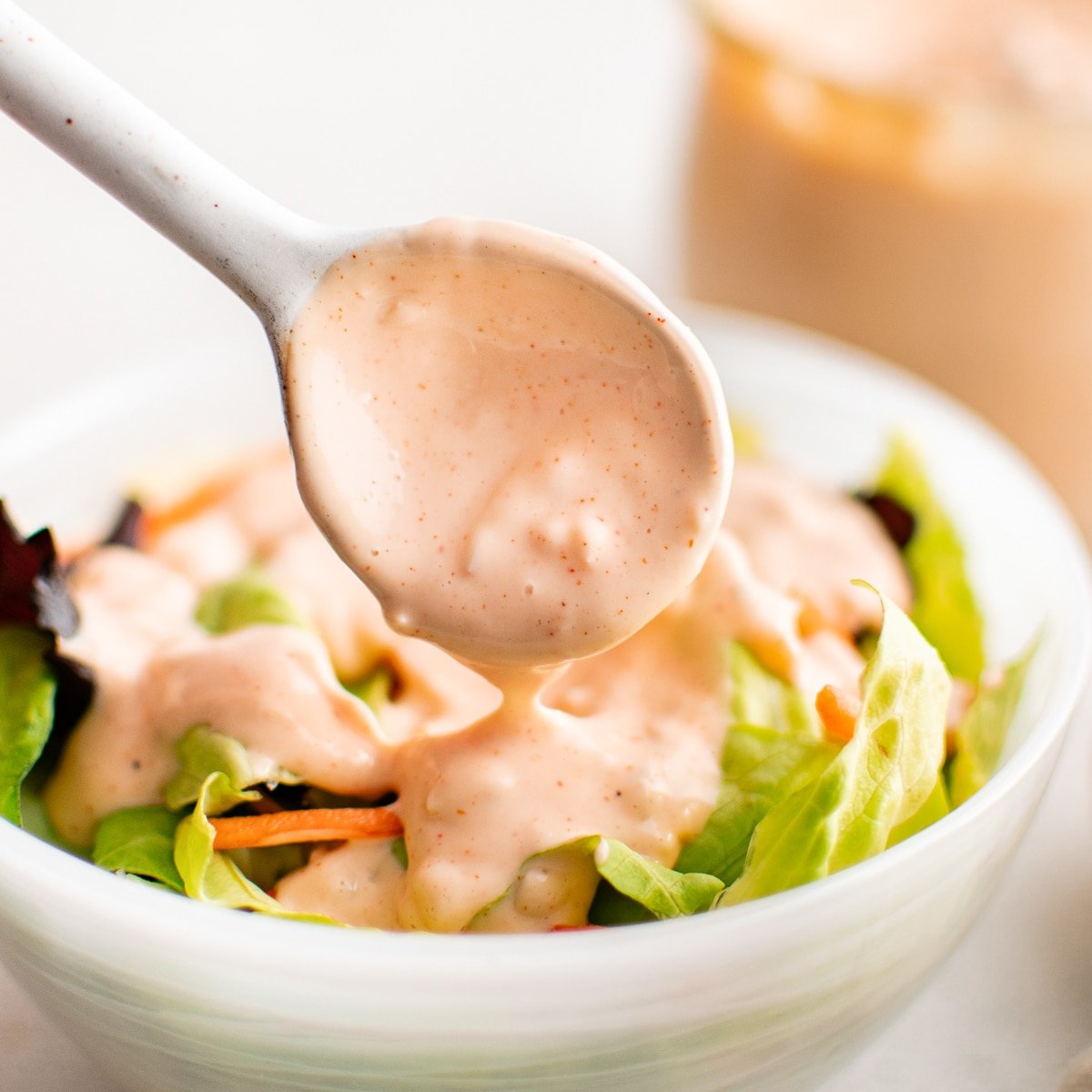 A spoonful of Thousand Island dressing being drizzled over a fresh green salad.