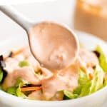 A spoonful of Thousand Island dressing being drizzled over a fresh green salad.