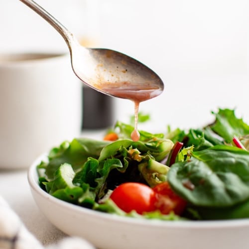 Spoon drizzling balsamic vinaigrette over a fresh salad
