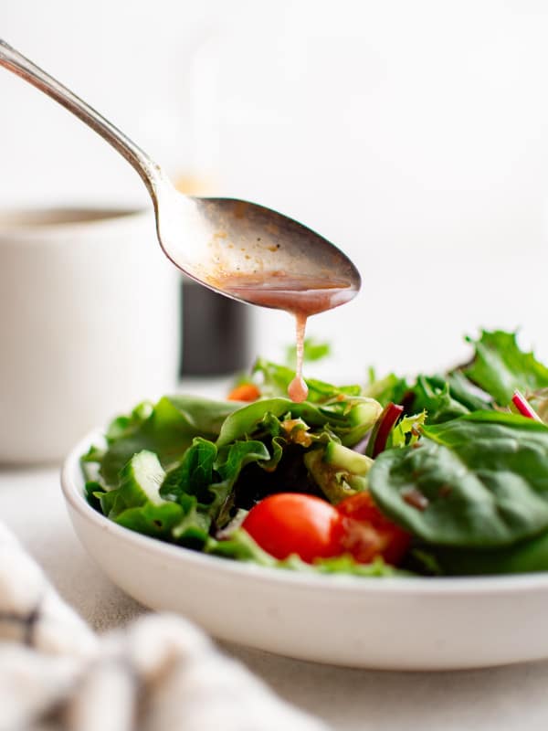 Spoon drizzling balsamic vinaigrette over a fresh salad