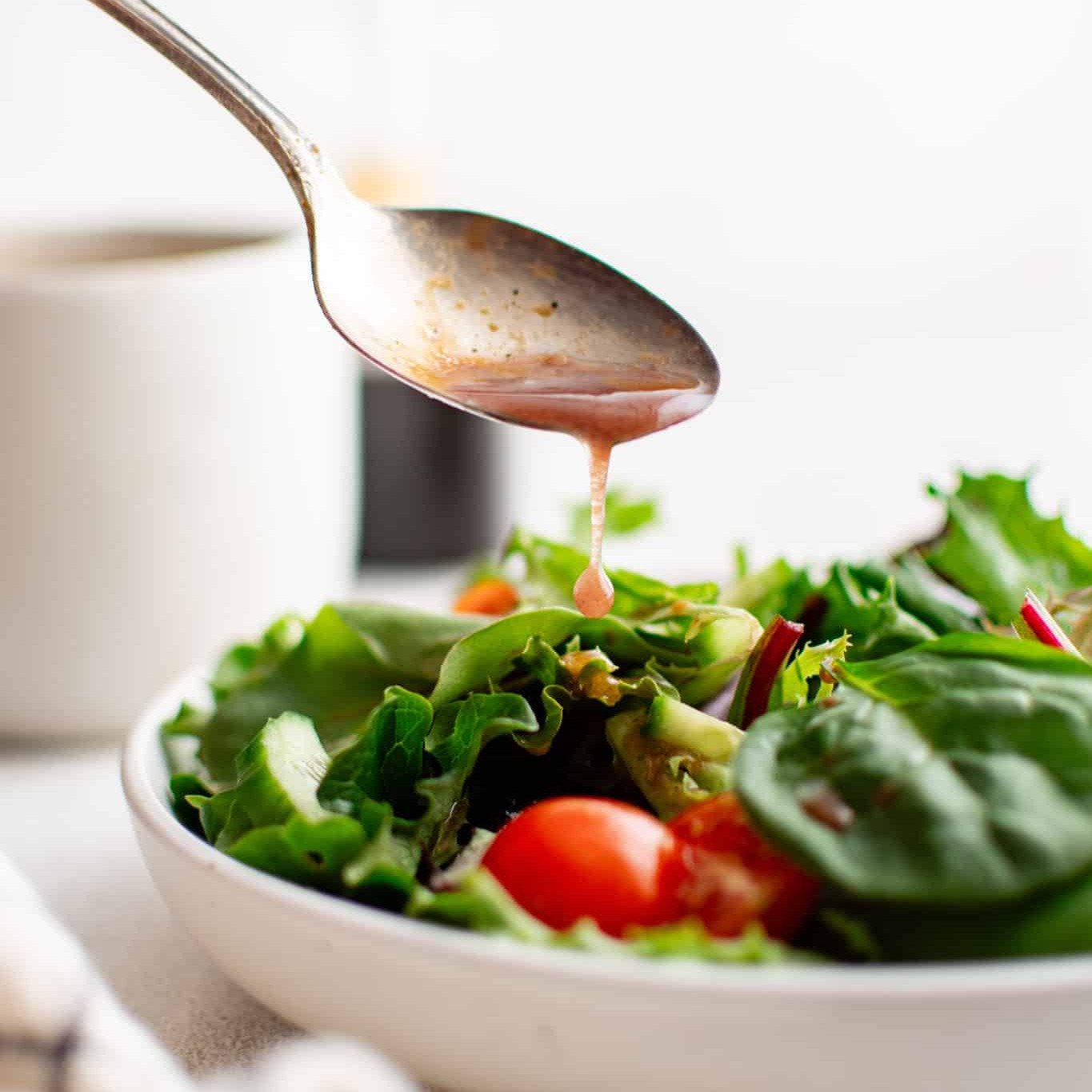 Spoon drizzling balsamic vinaigrette over a fresh salad