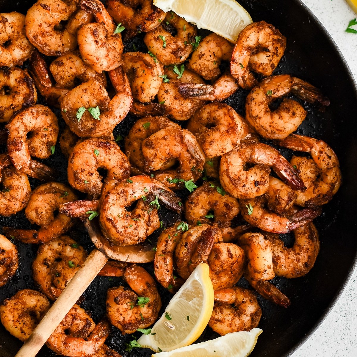op-down view of a skillet filled with golden blackened shrimp, garnished with chopped parsley and lemon wedges for a bright, fresh finish.