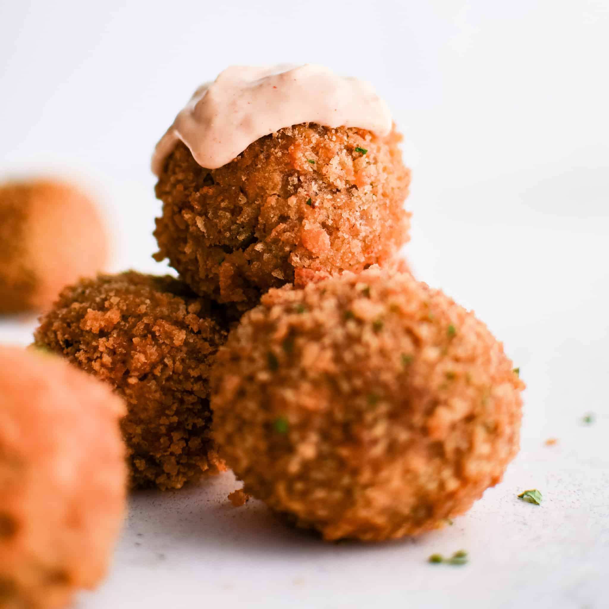 A minimalist, bright close-up of three boudin balls stacked casually, with one topped in sauce.