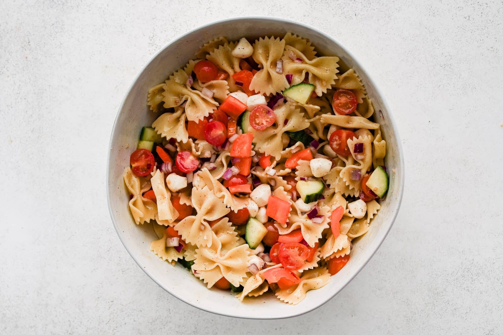 Large round mixing bowl filled with prepared bowtie pasta salad tossed in champagne vinaigrette.