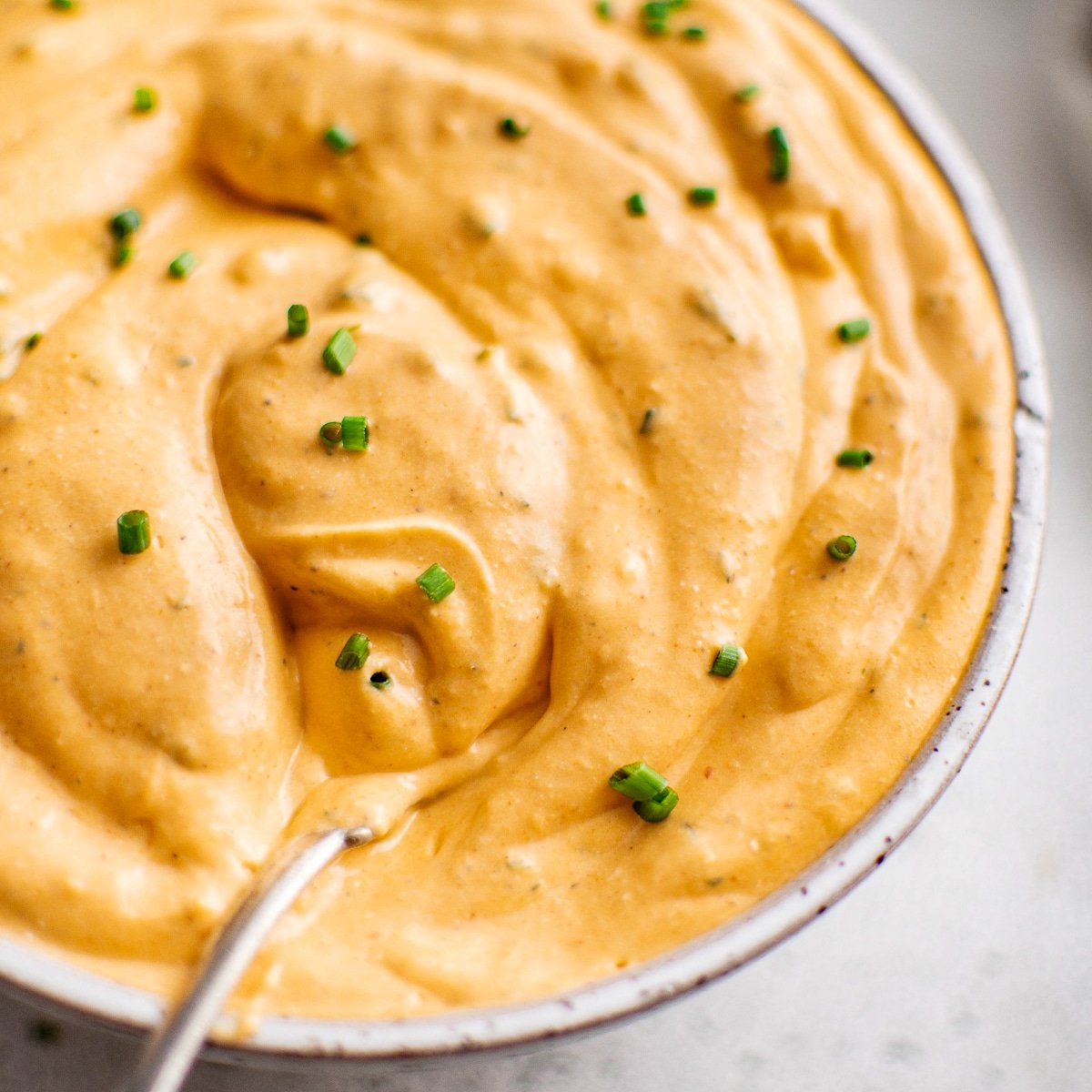A rich, thick buffalo ranch sauce swirled in a bowl, garnished with chopped chives, and a spoon ready for dipping.