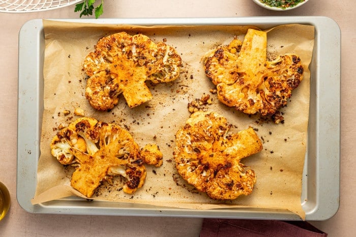 Golden roasted cauliflower steaks fresh from the oven on a parchment-lined baking sheet.