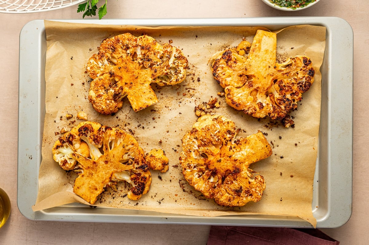 Golden roasted cauliflower steaks fresh from the oven on a parchment-lined baking sheet.