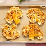 Four seasoned cauliflower steaks arranged on a parchment-lined baking sheet, ready to roast.