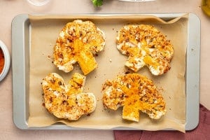 Four seasoned cauliflower steaks arranged on a parchment-lined baking sheet, ready to roast.