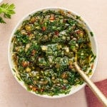 Overhead shot of vibrant homemade chimichurri sauce in a white bowl with a spoon.