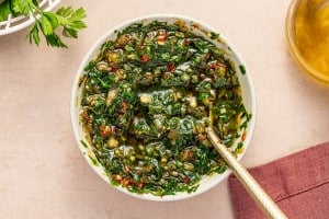 Overhead shot of vibrant homemade chimichurri sauce in a white bowl with a spoon.