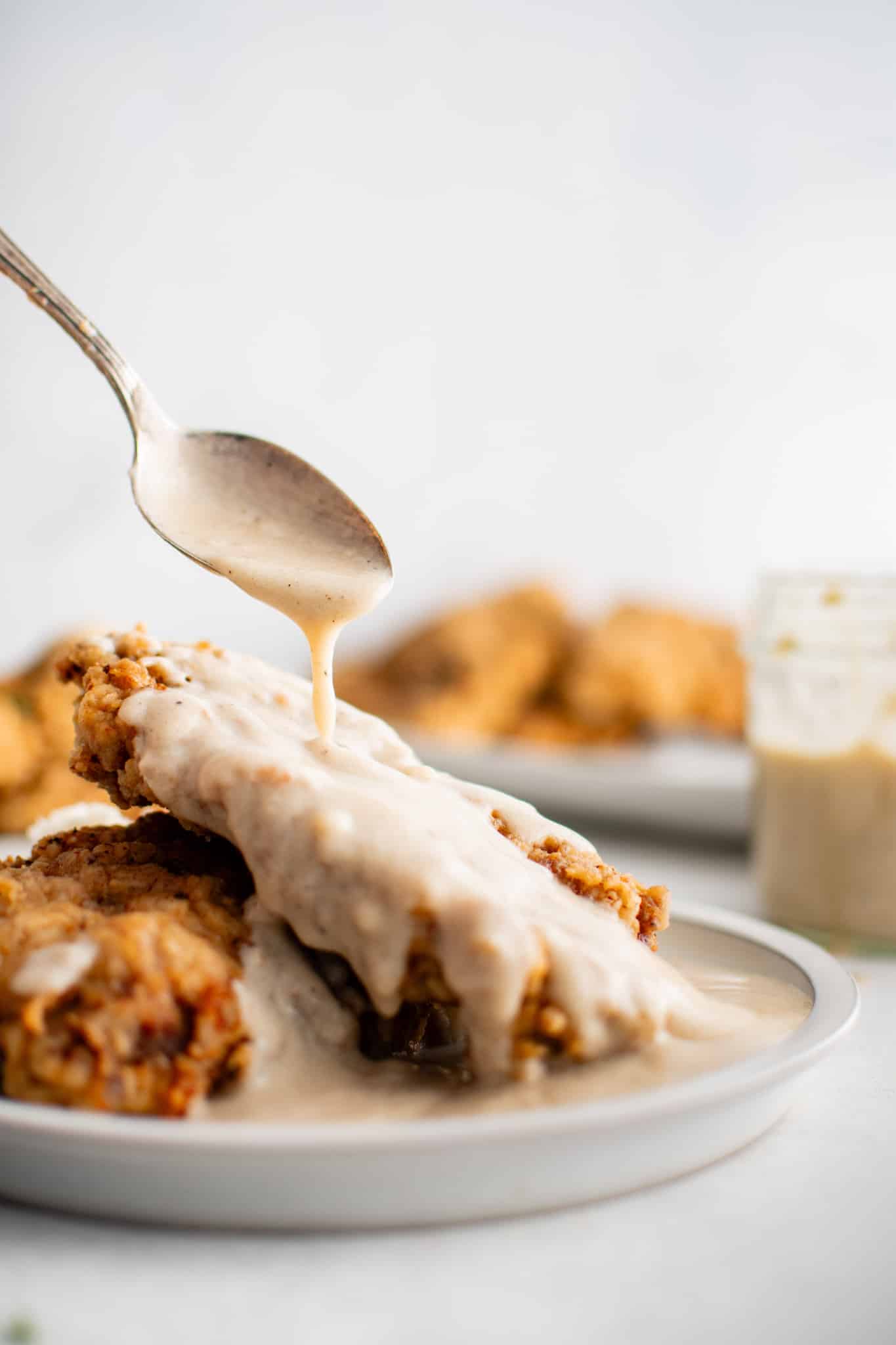A plate of golden fried steak being topped with a generous drizzle of homemade white gravy