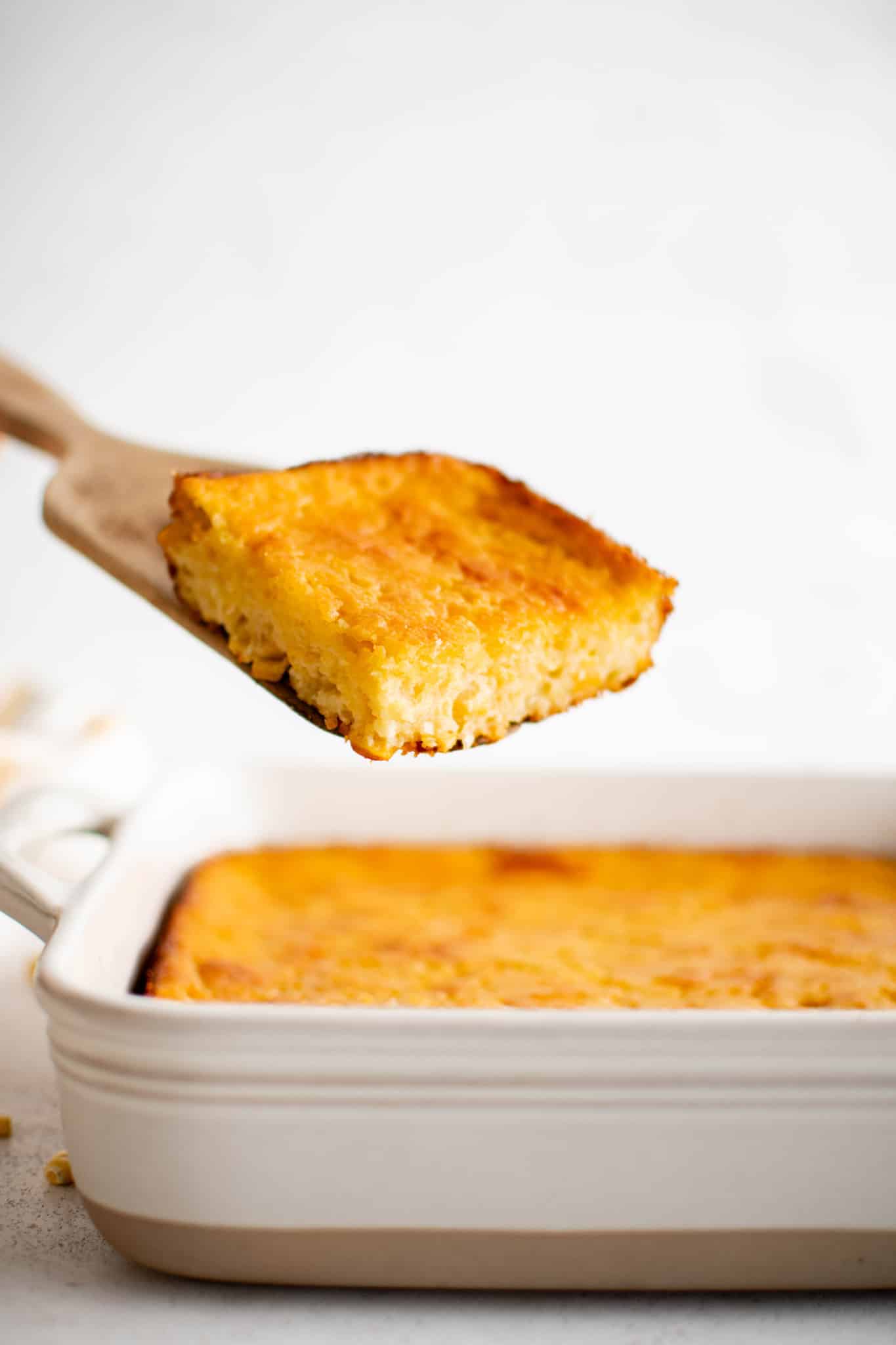 Slice of golden cornbread casserole being lifted from a white baking dish.