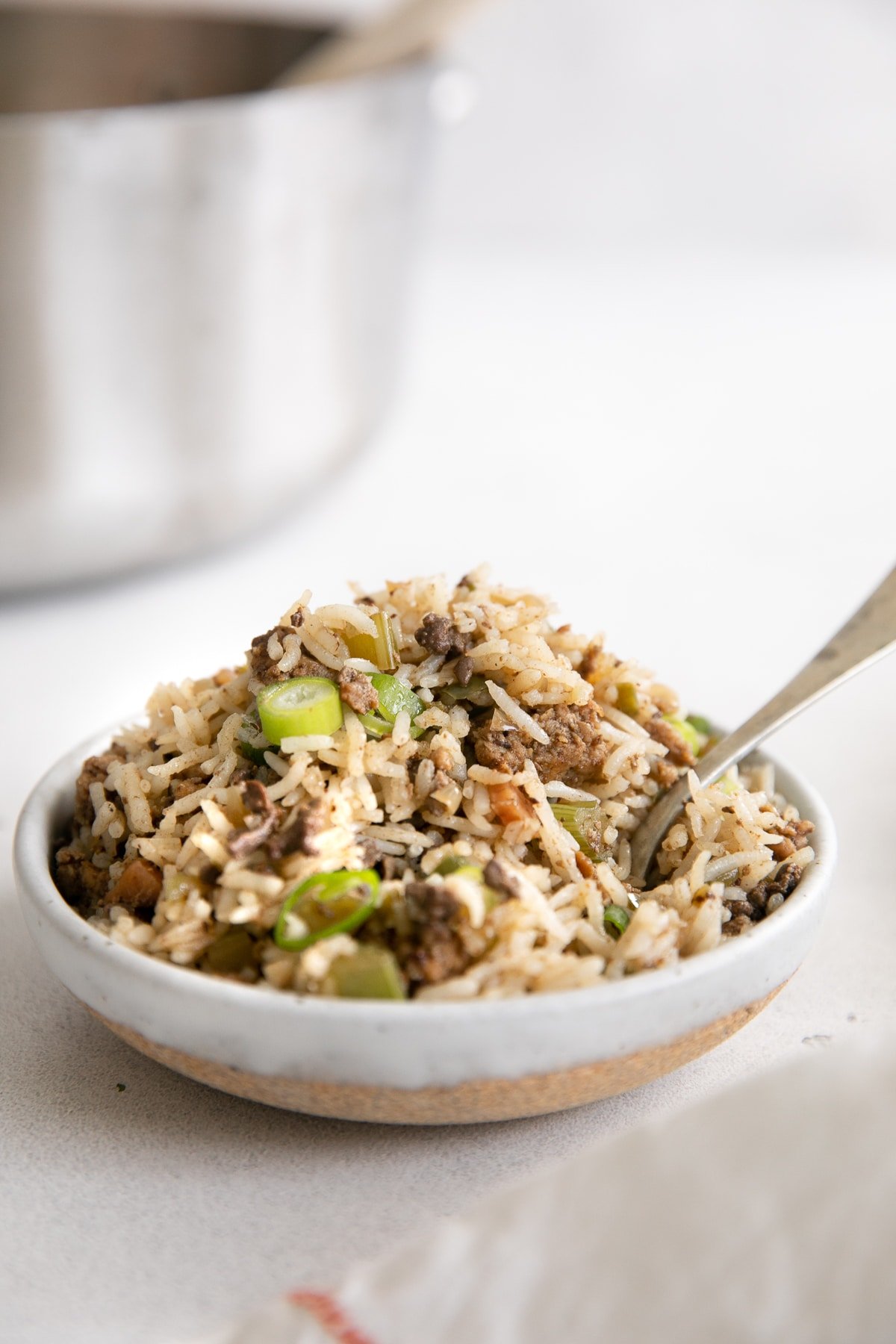 A rustic bowl filled with Cajun dirty rice, featuring seasoned ground beef, chopped peppers, and green onions, with a pot in the background.