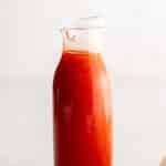 Clean vertical pin featuring a glass bottle filled with smooth, creamy French dressing in rich red-orange hues. Text overlay at the top reads โHomemade French Dressingโ on a neutral white background.