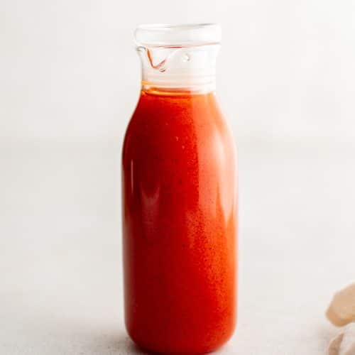 Front view of a glass bottle filled with freshly made French dressing, showing its smooth consistency and rich color against a light background.