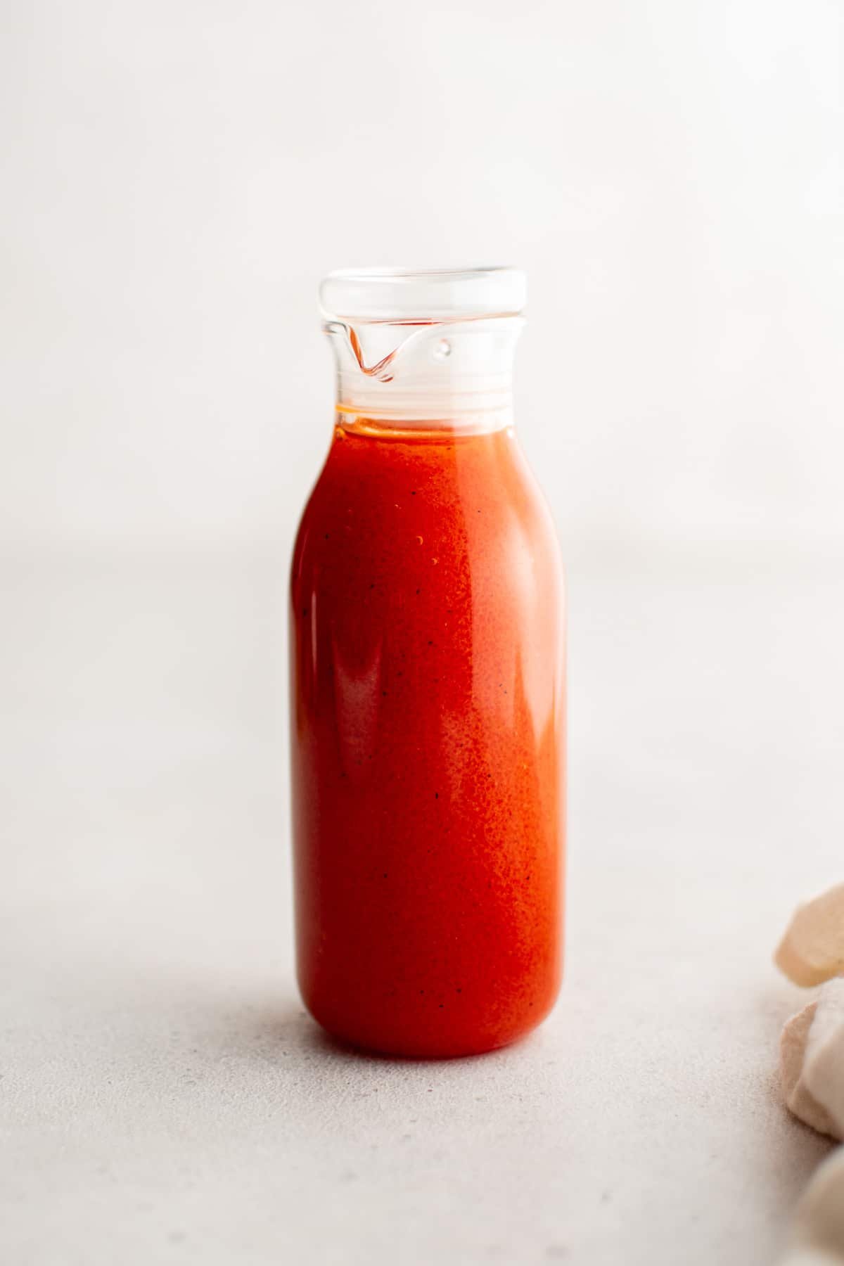 Front view of a glass bottle filled with freshly made French dressing, showing its smooth consistency and rich color against a light background.