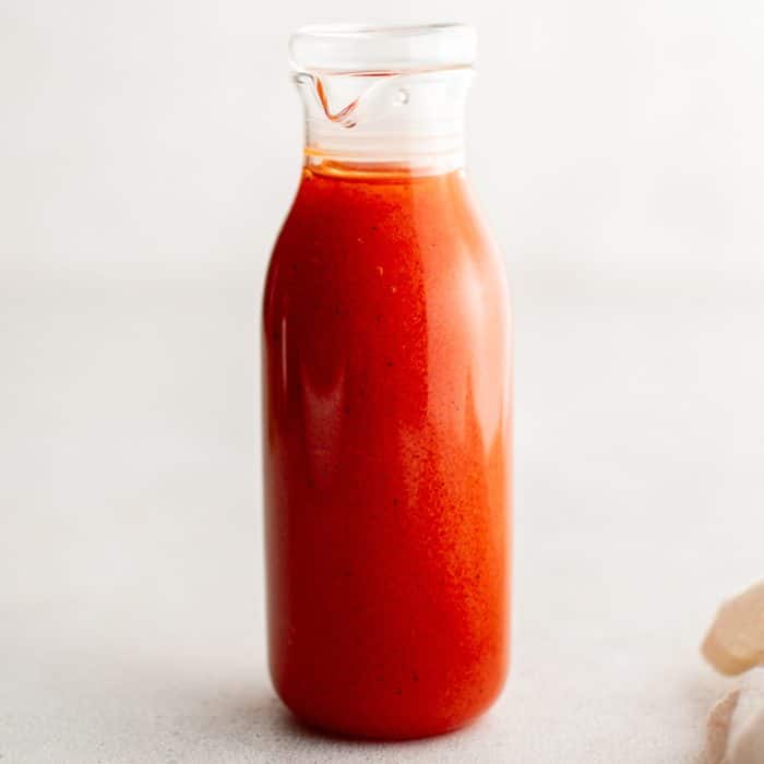 Centered square image of a clear glass bottle filled with creamy red-orange French dressing, ideal for recipe cards or thumbnails.