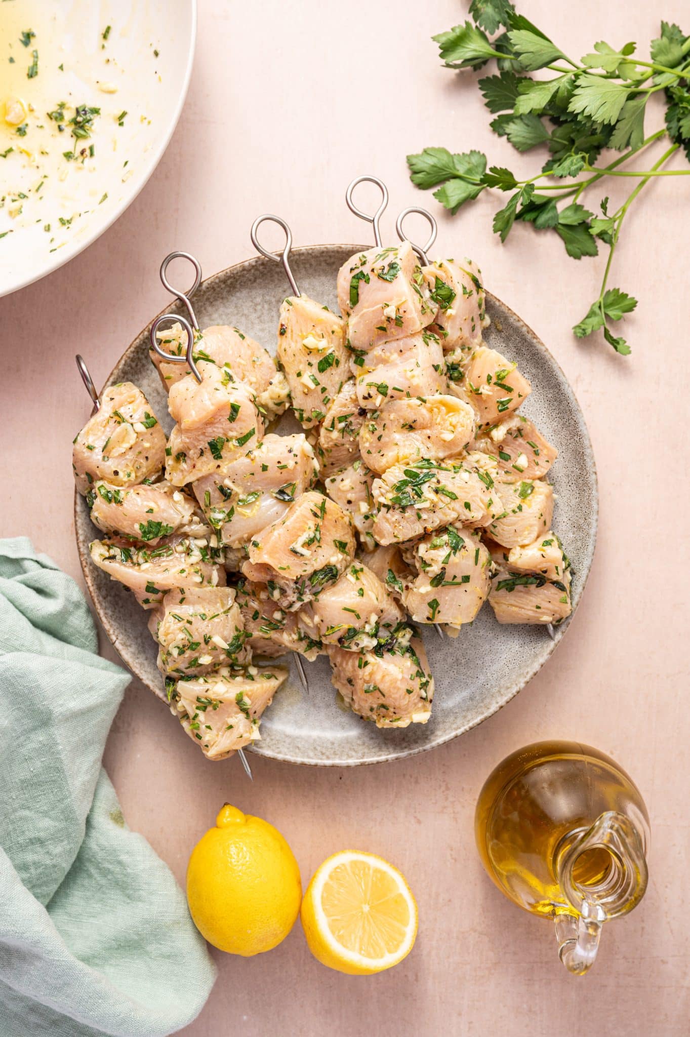 Chunks of raw chicken marinated in a lemon herb and olive oil mixture threaded onto metal skewers.