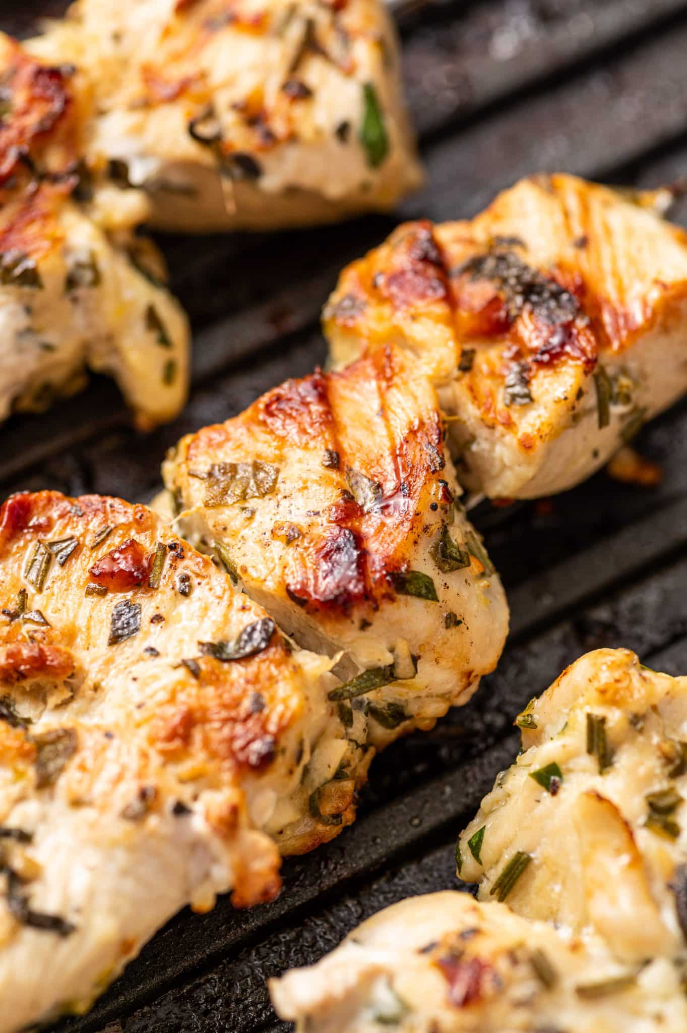 Close-up of juicy grilled chicken souvlaki skewers with golden grill marks, fresh herbs, and caramelized edges on a grill pan.