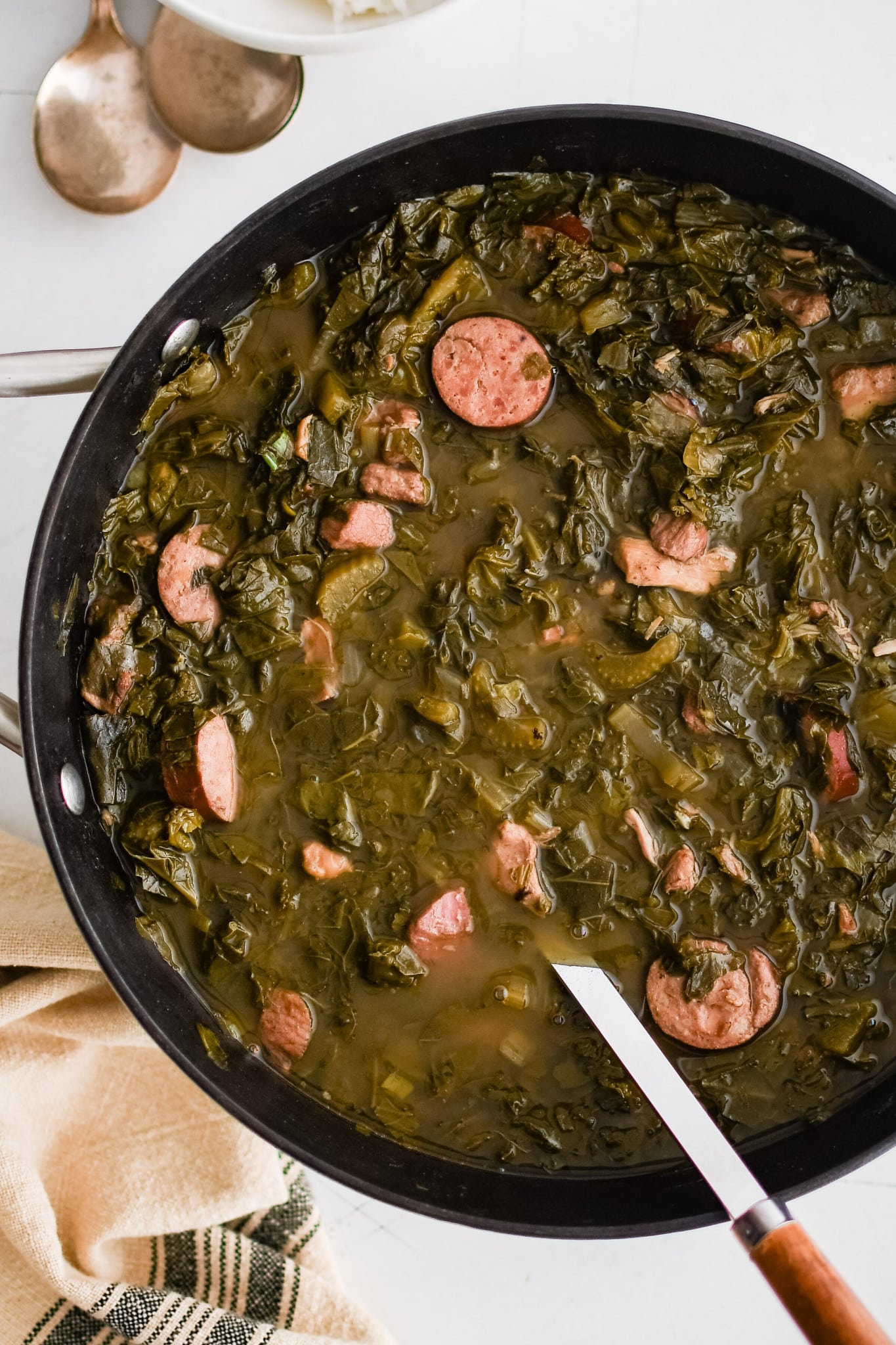 A skillet full of green gumbo, simmering with smoked sausage, collard greens, and a rich, savory broth.