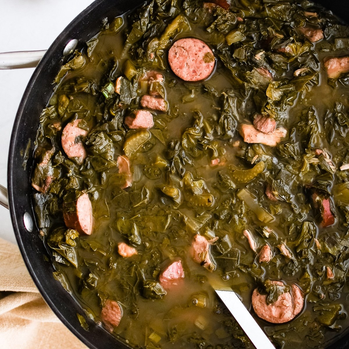 Green gumbo with sausage in pot next to bowl of rice