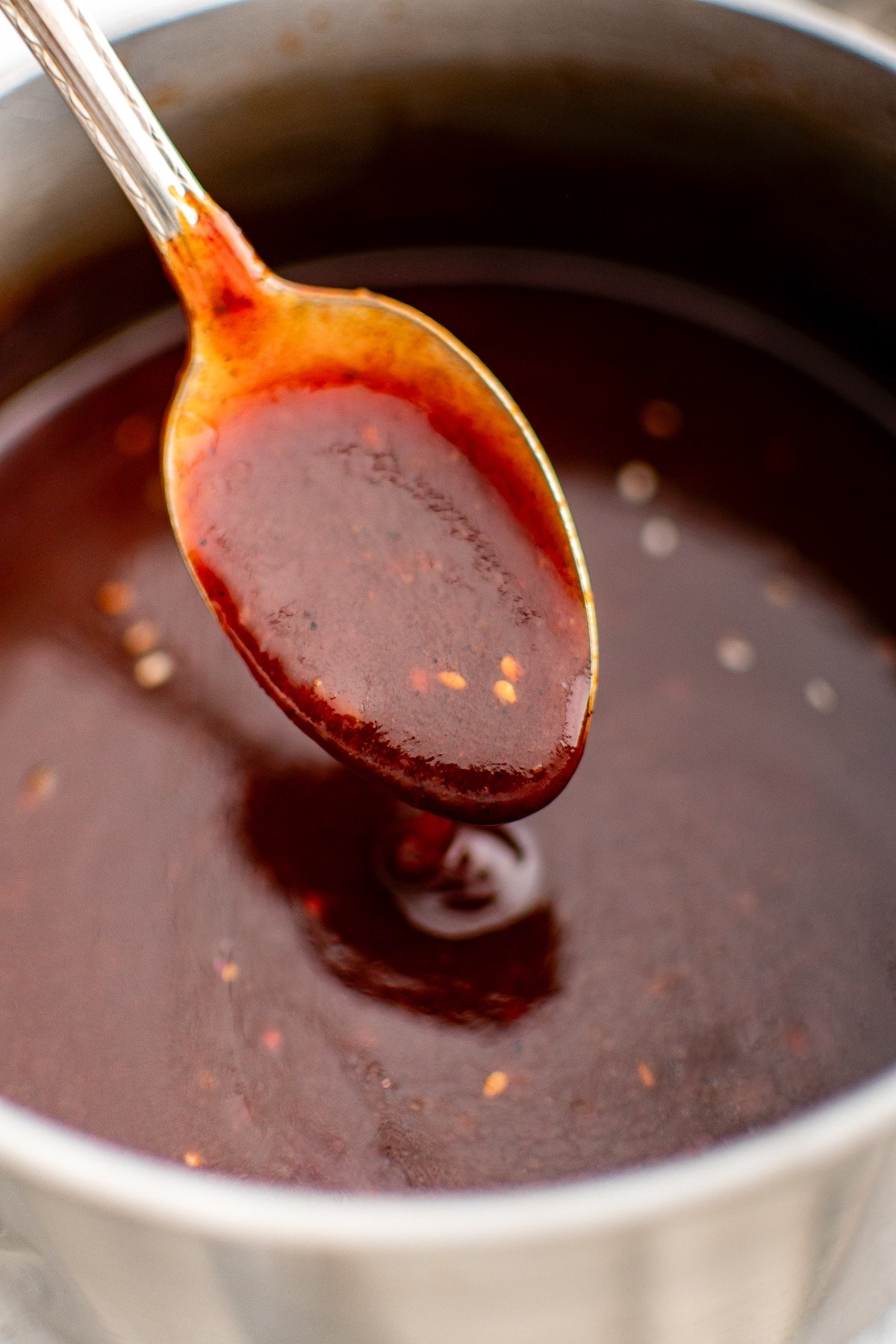A close-up of a spoonful of thickened Korean BBQ sauce lifted from the saucepan, showcasing its sticky, rich texture and flecks of sesame seed.