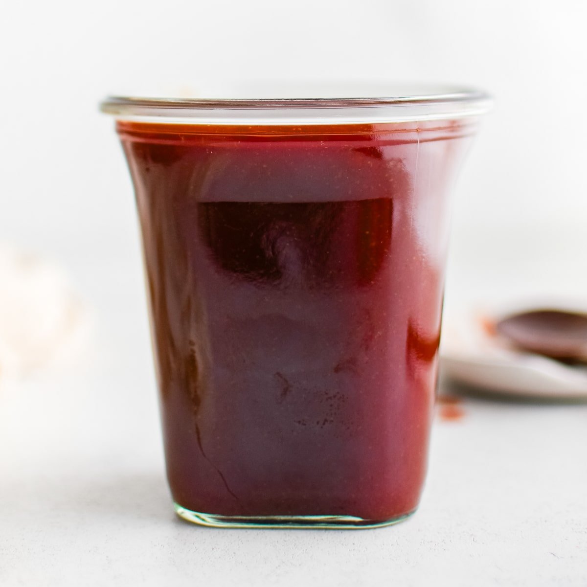 A focused, tight shot of a glass jar showcasing the rich red color and smooth texture of homemade mumbo sauce.