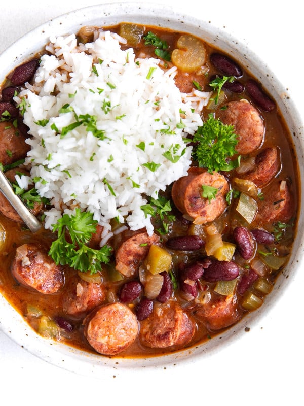 A hearty bowl of red beans stewed with smoked sausage, bell peppers, and onions, served alongside a generous scoop of fluffy white rice and garnished with parsley.