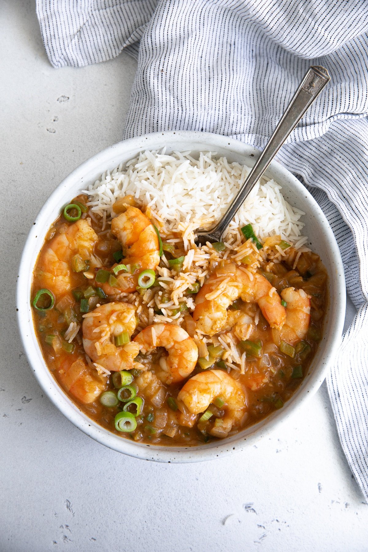 A bowl of classic shrimp étouffée served with fluffy white rice, topped with green onions, and set against a light background with a striped towel.