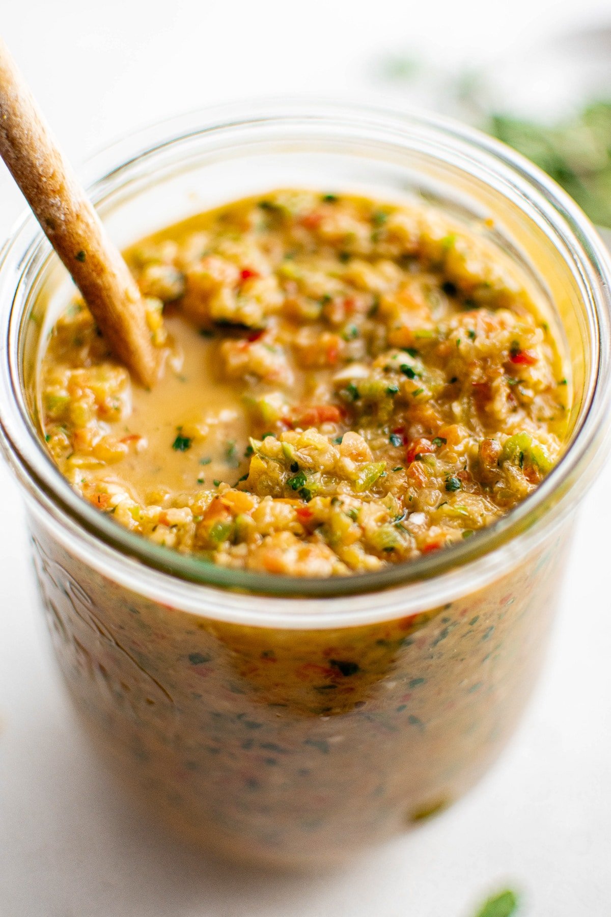 Jar filled with vibrant homemade sofrito with a wooden spoon resting inside