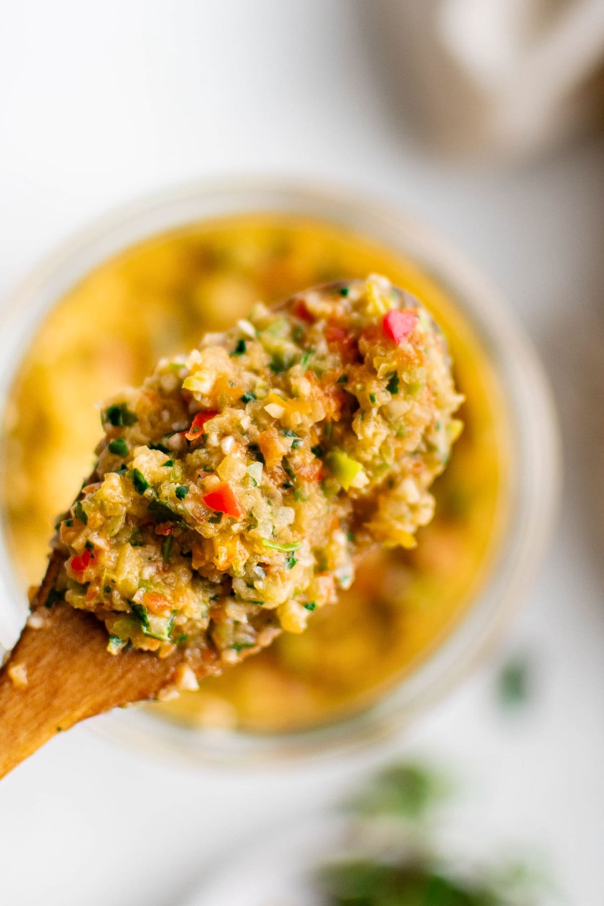 Overhead view of a spoonful of sofrito being lifted from a glass jar