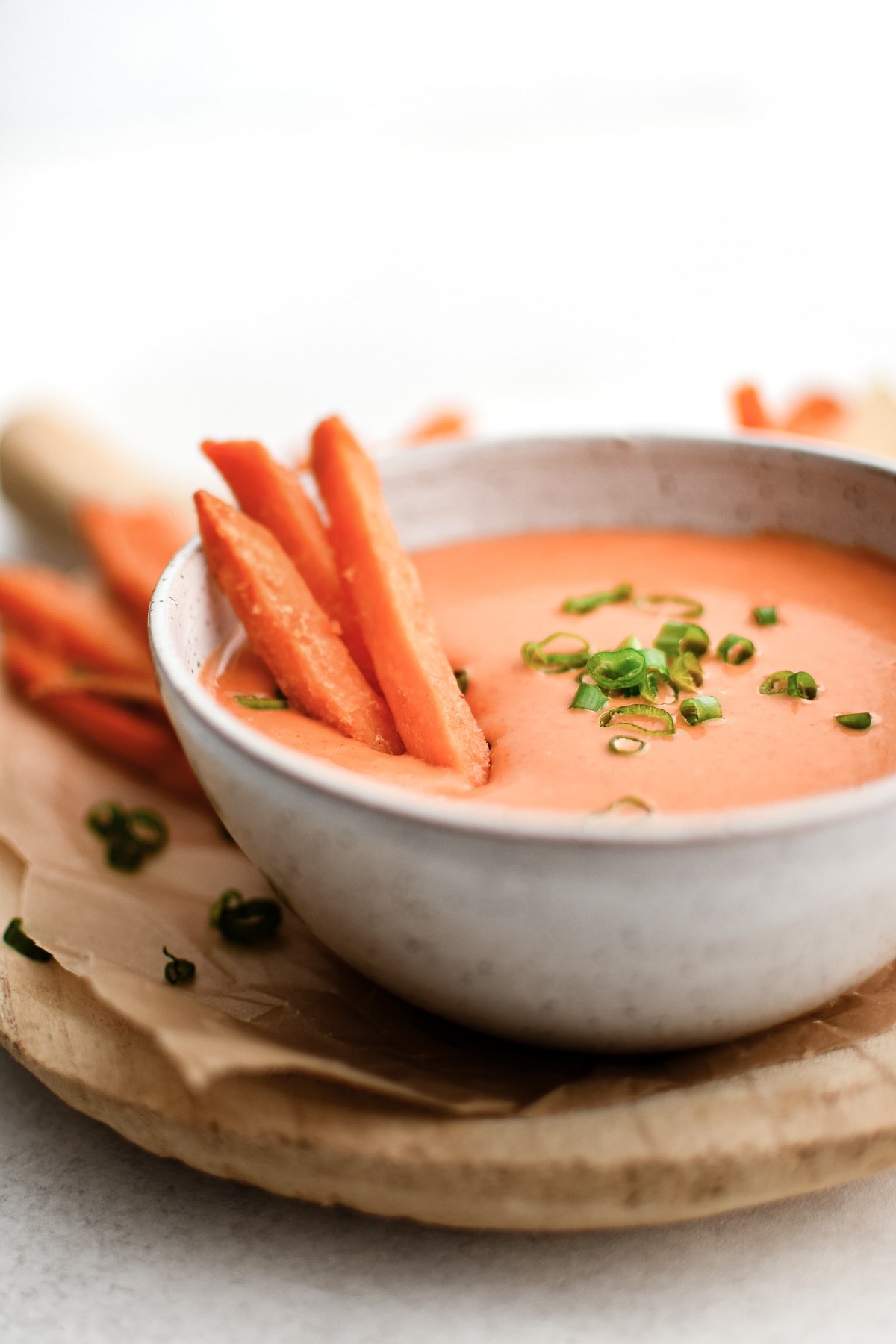 A bowl of spicy mayo garnished with chopped green onions and served with crispy sweet potato fries for dipping.