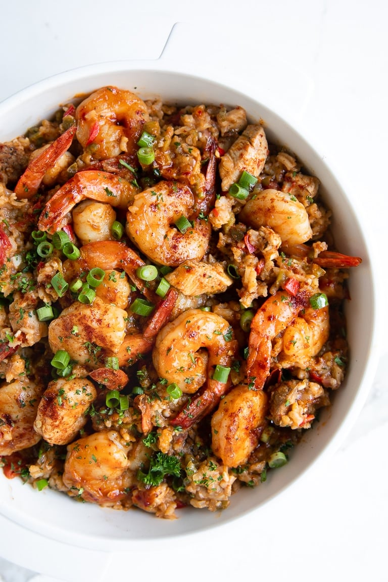 A vibrant bowl of Cajun jambalaya loaded with shrimp, chunks of chicken, and slices of sausage, garnished with chopped green onions and herbs.