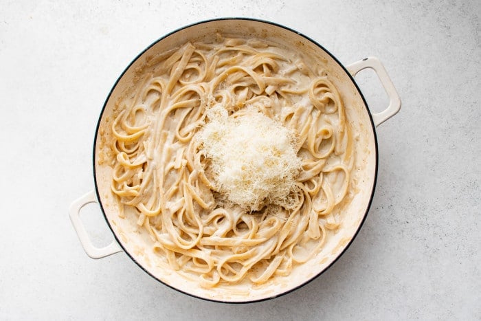 Freshly grated parmesan on top of creamy fettuccini pasta simmering in a large skillet.