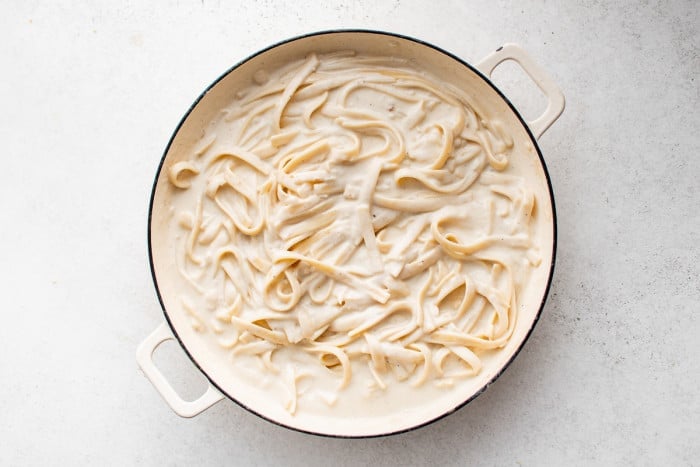 Fettuccini coated in creamy Alfredo sauce in a white skillet.