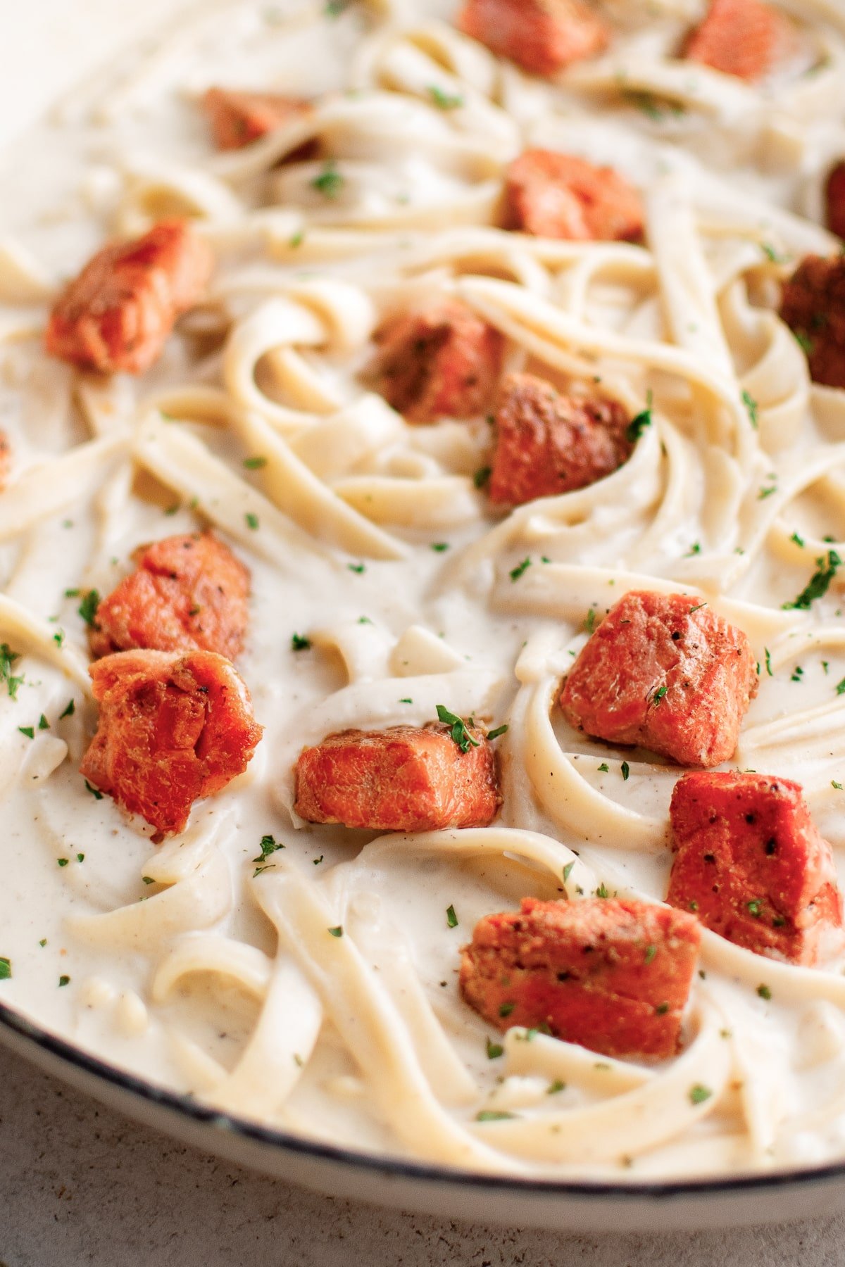 A detailed view of the creamy fettuccini pasta with seared Cajun salmon bites nestled throughout and a touch of fresh herbs.